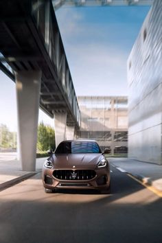 the front end of a brown sports car driving down a street next to a tall building