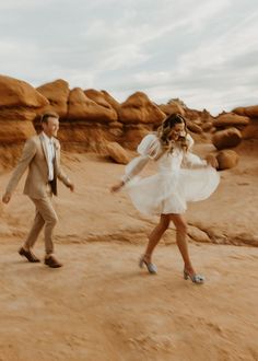 a man and woman are walking in the desert with their dress blowing in the wind