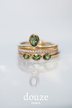 two gold rings with green and white stones on them, one is in the shape of a heart