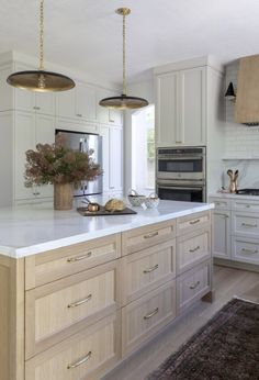 a large kitchen with white cabinets and an island in the middle is lit by two pendant lights