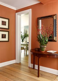 an orange room with pictures on the wall and a vase full of flowers in it