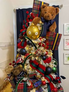 a teddy bear sitting on top of a christmas tree decorated with plaid ribbon and ornaments