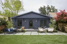 an outdoor patio with chairs and tables in front of a gray building surrounded by greenery