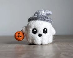 a small white stuffed animal with a gray hat on it's head and a button in its mouth