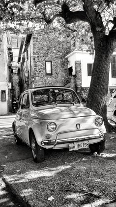 an old car parked in front of a tree on the side of the road next to a building