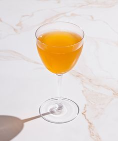 a glass filled with orange juice sitting on top of a white marble countertop next to a spoon