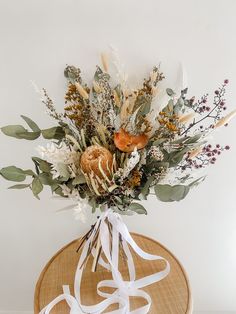 a bouquet of flowers on top of a round wooden table with white ribbon around it