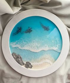 two dolphins swimming in the ocean through a round glass frame on a bed with white sheets