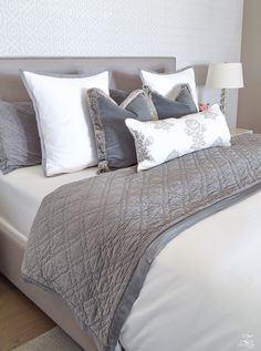 a bed with white and grey pillows on it's headboard, in a bedroom