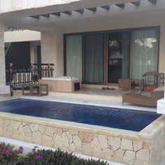 an outdoor swimming pool in front of a house with patio furniture and large sliding glass doors