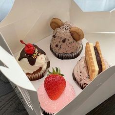 four cupcakes in a box with chocolate frosting and strawberries