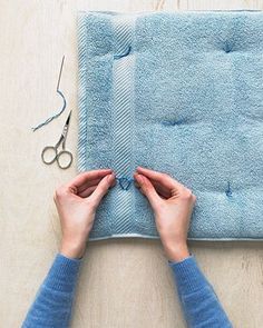 someone using scissors to cut the edge of a piece of blue fabric with yarn on it