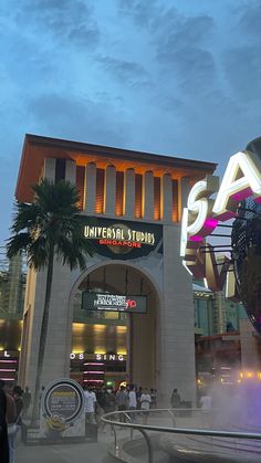 the entrance to universal studios at night with palm trees and people walking around in front