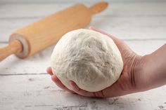 a person holding a ball of dough next to a rolling pin