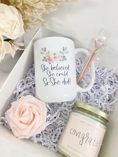 a white coffee mug sitting on top of a table next to a candle and some flowers