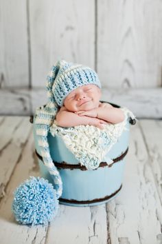 a newborn baby in a bucket with a hat and pom - pom