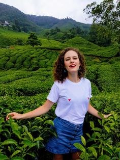 a woman standing in the middle of a lush green field with her arms outstretched out