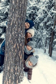 a group of people standing next to a tree in the snow