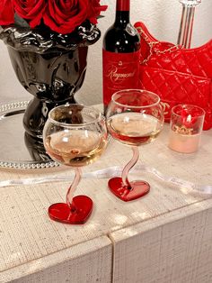 two wine glasses sitting on top of a table next to a vase filled with red roses