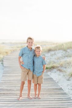 two young boys standing on a boardwalk in the sand