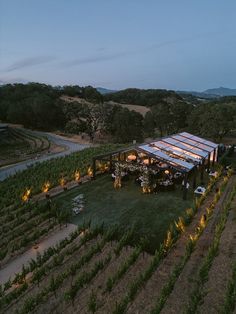 an aerial view of a winery at night with lights on the roof and rows of vines in the foreground