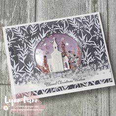 a card with a white church on it and snowflakes around the edges, in front of a wooden background