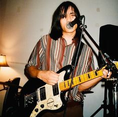 a man with long hair playing an electric guitar in front of a microphone and lamp