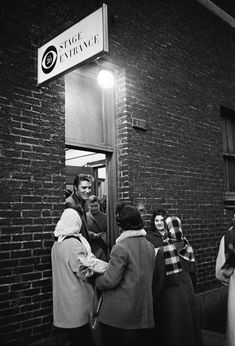 black and white photograph of people standing in front of a brick building with a sign on it