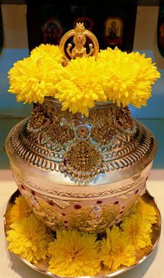 a silver vase with yellow flowers and a gold crown on it's top sitting on a plate