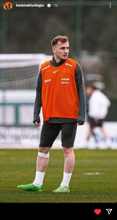 a man standing on top of a soccer field wearing an orange and black uniform with white socks