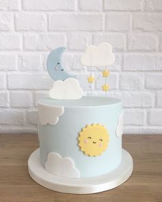 a blue cake decorated with clouds, sun and moon on top is sitting in front of a white brick wall