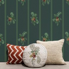 two pillows and a decorative pillow on a table in front of a wallpapered background