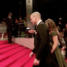 a man and woman walking down a red carpeted area in front of an audience