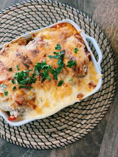 a casserole dish with meat, cheese and parsley on a wicker plate