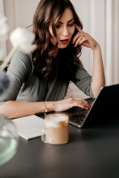 a woman sitting at a table with a laptop computer in front of her and looking at the screen