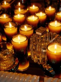 many candles are lit on a table with clear glass vases filled with white candles