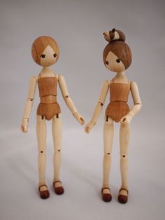 two wooden dolls standing next to each other on a white surface with one holding the hand of another doll