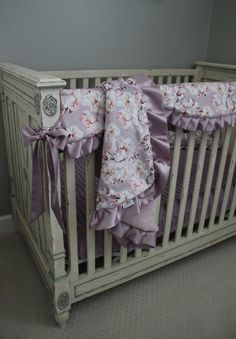 a baby crib with purple ruffles and bows on the bedding is shown