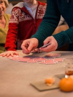 a woman cutting up some cards on top of a table with other people sitting around