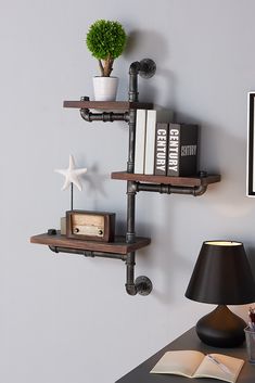 two industrial pipe shelves are mounted to the wall above a desk with a lamp and books on it