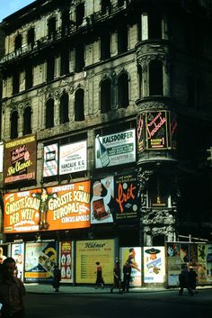 an old building with many advertisements on it's sides and people walking down the street