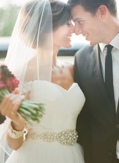 a bride and groom smile at each other as they hold their bouquets in front of them