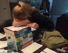 a person leaning their head on some books while sitting at a table with other items