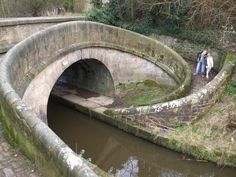 two people standing on the side of a bridge over a river with a stone arch