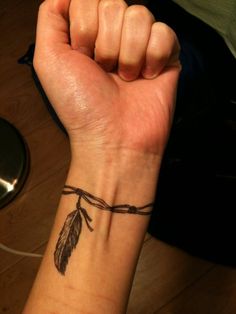 a woman's wrist tattoo with a feather on it and a string attached to the wrist