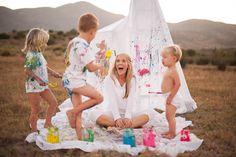 a woman sitting on top of a blanket next to two children in front of a teepee