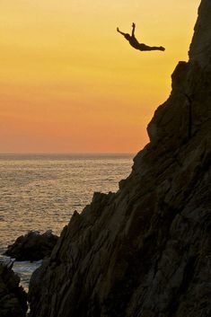 a person jumping off the side of a cliff into the ocean