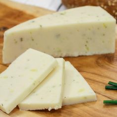 several pieces of cheese sitting on top of a wooden cutting board next to green sticks