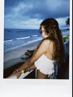 a woman standing on top of a balcony next to the ocean in front of a cloudy sky