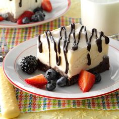 two slices of cheesecake with chocolate sauce and berries on the plate next to a glass of milk